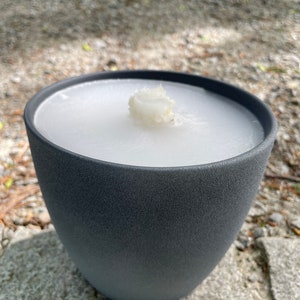 May include: A gray ceramic candle holder with a white candle inside. The candle is partially melted.
