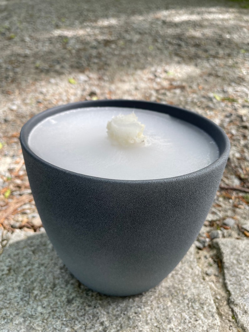 May include: A gray ceramic candle holder with a white candle inside. The candle is partially melted.