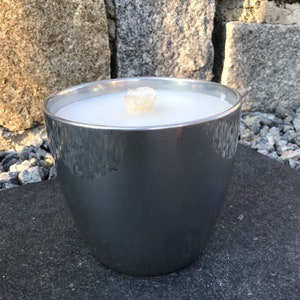 May include: A silver metal candle holder with a white candle inside. The candle is lit and the wick is visible.