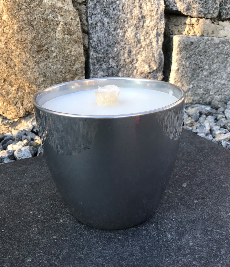 May include: A silver metal candle holder with a white candle inside. The candle is lit and the wick is visible.