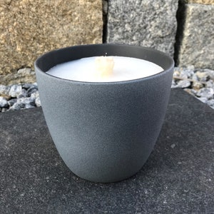 May include: A gray ceramic candle holder with a white candle inside. The candle is lit and the flame is visible.