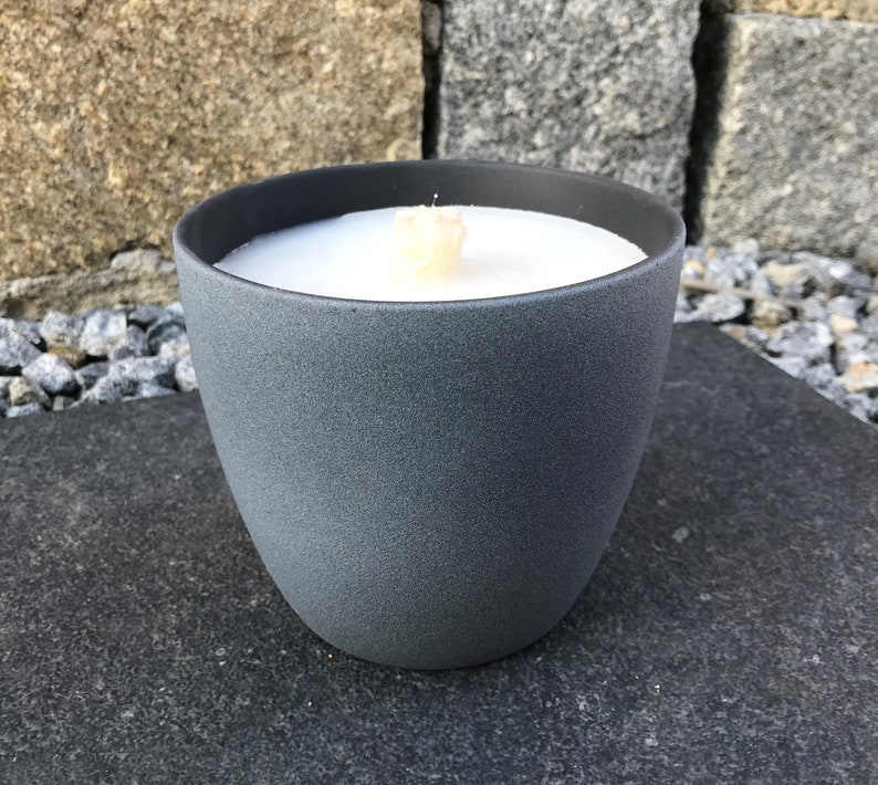 May include: A gray ceramic candle holder with a white candle inside. The candle is lit and the flame is visible.