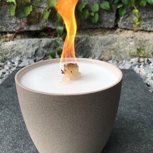 May include: A beige ceramic candle holder with a white wax candle and a wooden wick burning with a bright orange flame.