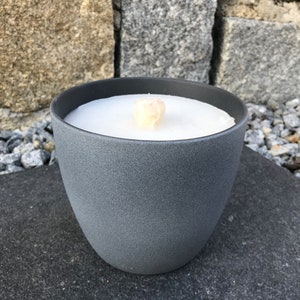 May include: A gray ceramic candle holder with a white candle inside. The candle has a wooden wick.
