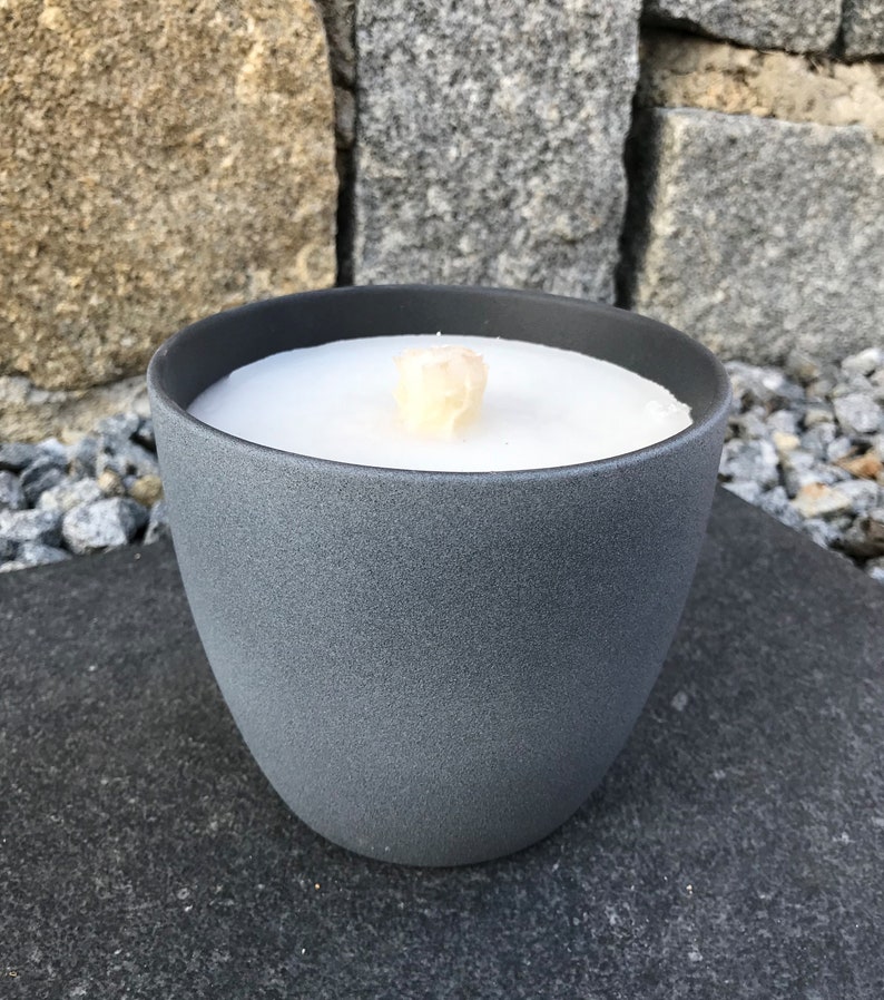 May include: A gray ceramic candle holder with a white candle inside. The candle has a wooden wick.
