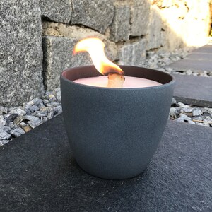 May include: A gray ceramic candle holder with a lit candle inside. The candle is a light pink color and the flame is orange.