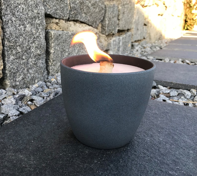 May include: A gray ceramic candle holder with a lit candle inside. The candle is a light pink color and the flame is orange.