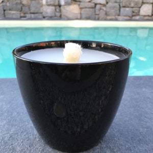 May include: A black ceramic candle holder with a white candle inside. The candle is lit and the flame is visible. The candle holder is sitting on a gray surface.