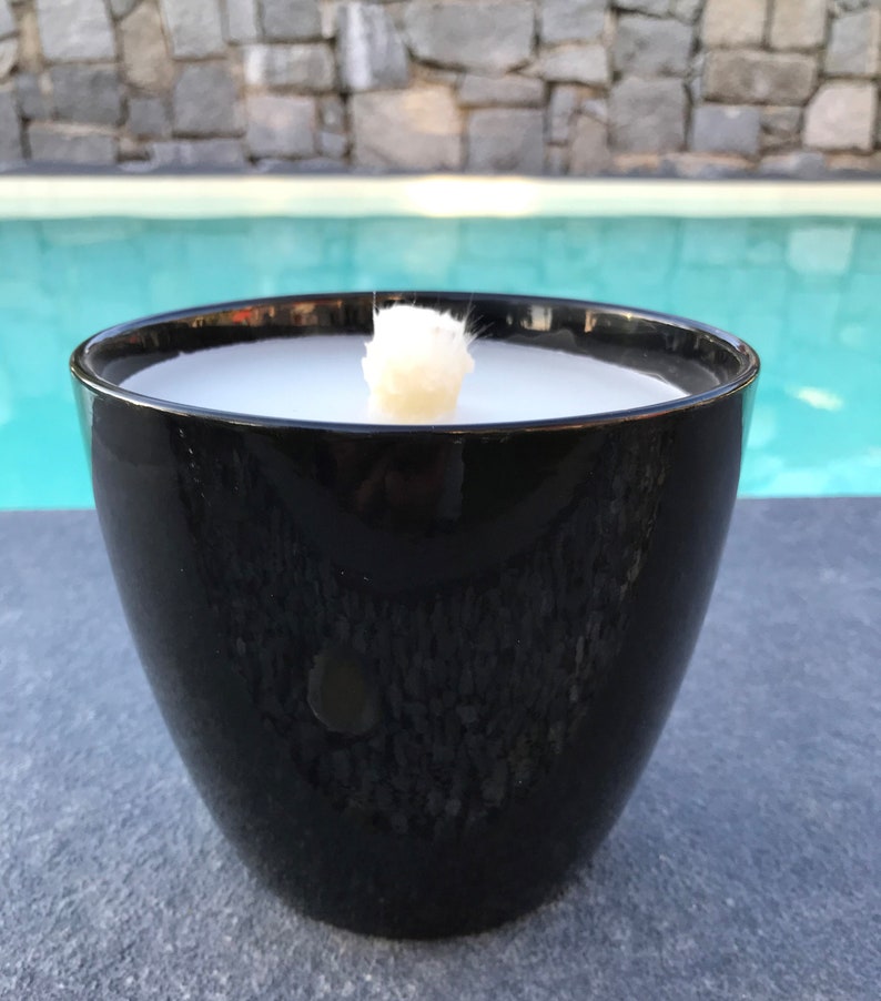 May include: A black ceramic candle holder with a white candle inside. The candle is lit and the flame is visible. The candle holder is sitting on a gray surface.