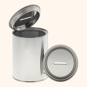 Könnte beinhalten: Eine weiße Keramiktasse mit schwarzem Henkel und dem Text "But First, Coffee" in fetter, schwarzer Schrift. Die Tasse steht vor einem verschwommenen Hintergrund, der eine gemütliche Umgebung suggeriert.