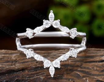 May include: A delicate, silver ring enhancer with a marquise and round diamond design. The enhancer is shaped like a V and features a cluster of diamonds at the point.
