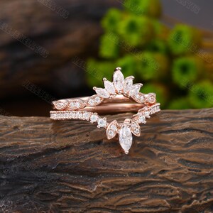 May include: Rose gold wedding band set with a delicate marquise-shaped diamond crown design. The band features a row of smaller diamonds.