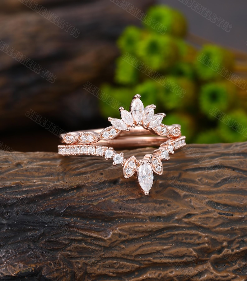 May include: Rose gold wedding band set with a delicate marquise-shaped diamond crown design. The band features a row of smaller diamonds.