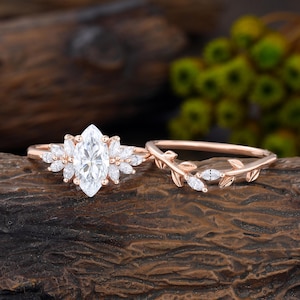 Può includere: Un set di anelli in oro rosa con una pietra bianca centrale taglio marquise circondata da pietre più piccole taglio marquise, abbinato a una fede coordinata con un motivo a tralcio che incastona piccole pietre taglio marquise in oro rosa.