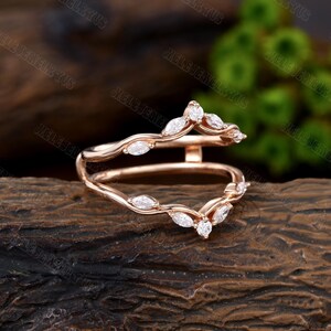 May include: A rose gold ring with a delicate, curved design. The ring is set with marquise-shaped diamonds, which are arranged in a pattern that resembles a vine. The ring is a beautiful and elegant piece of jewelry.