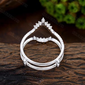 May include: A silver ring with a V-shaped design and small diamonds. The ring is designed to be worn as a wedding band or engagement ring.