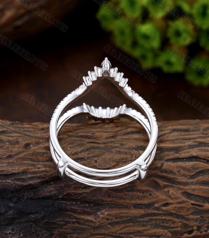 May include: A silver ring with a V-shaped design and small diamonds. The ring is designed to be worn as a wedding band or engagement ring.