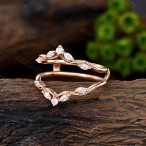May include: Rose gold ring with a delicate marquise diamond design. The ring is a split shank style, with two bands that meet at the top to create a V-shape. The diamonds are set in a pave setting, and the ring has a polished finish.