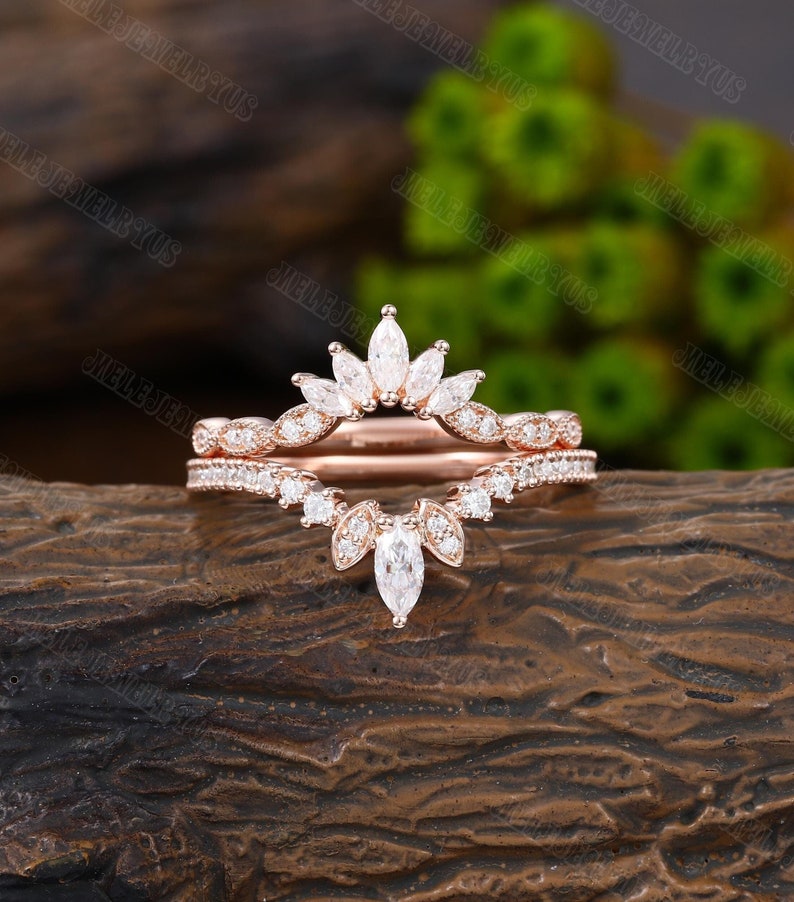 May include: A rose gold wedding band set with a marquise-shaped diamond crown and a delicate band of smaller diamonds.