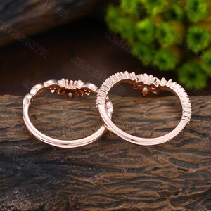 May include: Two rose gold rings with a delicate floral design and small clear stones. The rings are on a wooden surface.