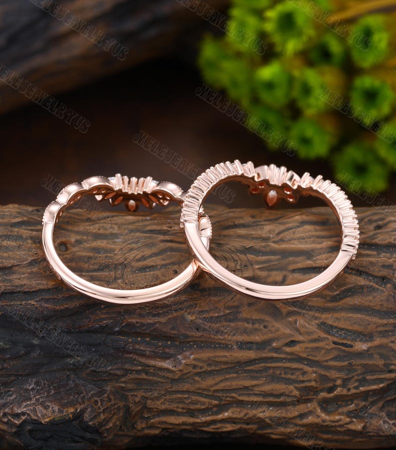 May include: Two rose gold rings with a delicate floral design and small clear stones. The rings are on a wooden surface.
