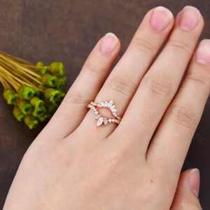 May include: Rose gold wedding band with a marquise shaped diamond setting. The band is adorned with smaller diamonds.