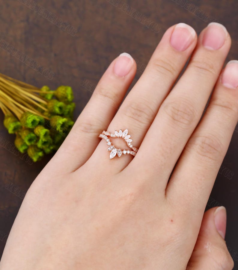 May include: Rose gold wedding band with a marquise shaped diamond setting. The band is adorned with smaller diamonds.