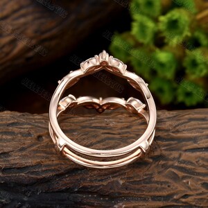 May include: Rose gold double band engagement ring with a delicate floral design and small round stones. The ring is shown from the back, showcasing the double band construction.
