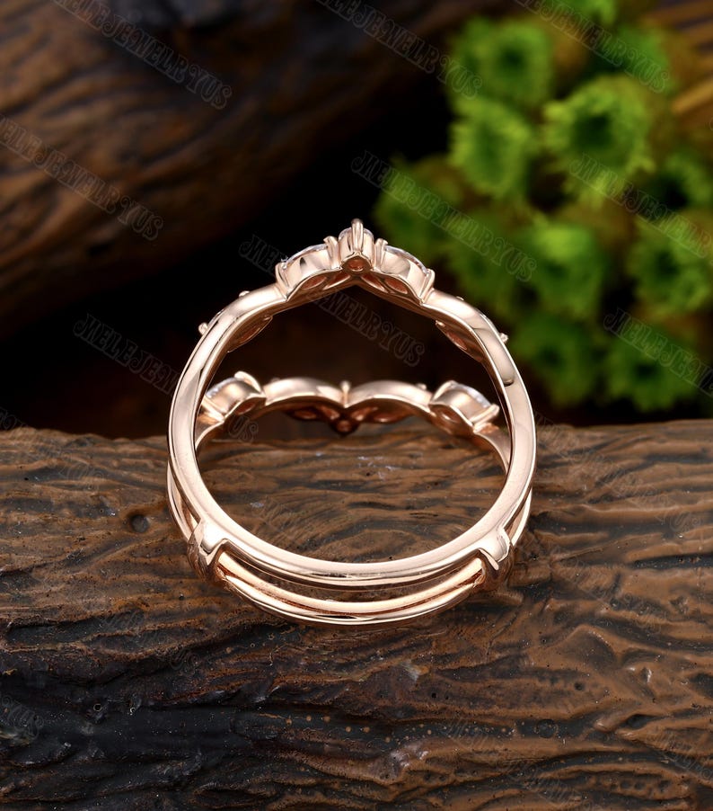 May include: Rose gold double band engagement ring with a delicate floral design and small round stones. The ring is shown from the back, showcasing the double band construction.