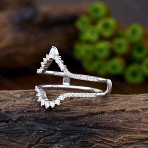 May include: A delicate, silver ring with a V-shaped design. The ring is set with small, sparkling diamonds. The ring is designed to be worn as a wedding band or an engagement ring.