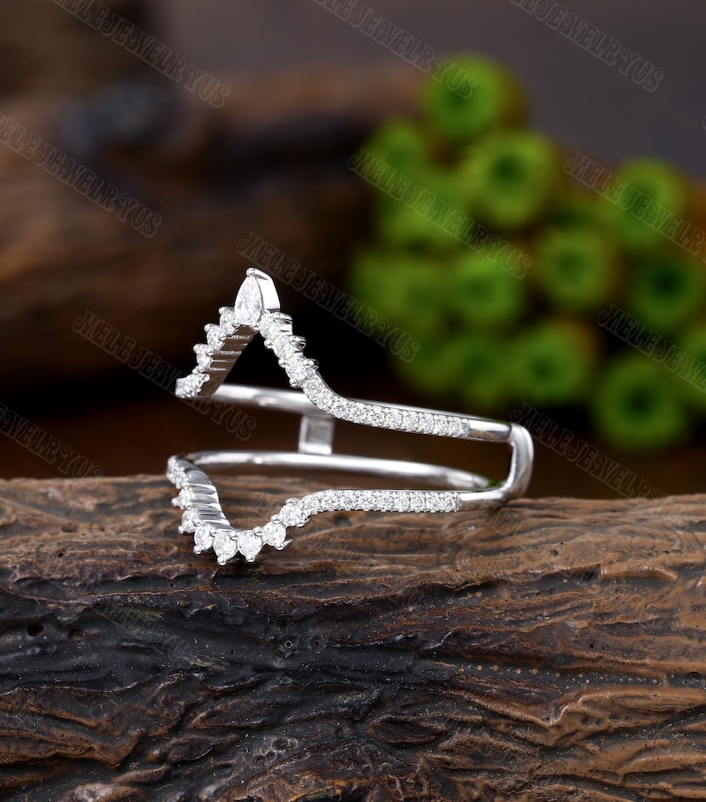 May include: A delicate, silver ring with a V-shaped design. The ring is set with small, sparkling diamonds. The ring is designed to be worn as a wedding band or an engagement ring.