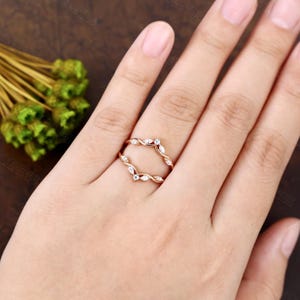 May include: A delicate rose gold ring with a twisted design and small diamonds set in a leaf pattern. The ring is designed to be worn as a wedding band enhancer.