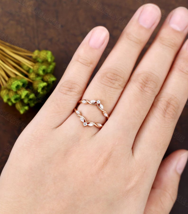 May include: A delicate rose gold ring with a twisted design and small diamonds set in a leaf pattern. The ring is designed to be worn as a wedding band enhancer.