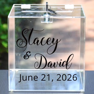 May include: Clear acrylic box with a slot on top and a lock with keys. The front of the box has the names "Stacey & David" and the date "June 21, 2026" in black script.