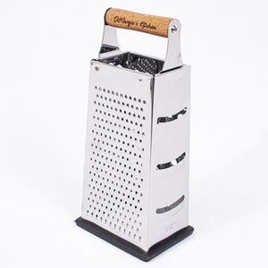 Peut inclure: Une râpe à boîte en argent à quatre côtés avec une poignée en bois. La poignée est gravée du texte "DiMaggio's Kitchen".