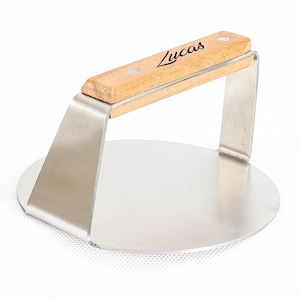 May include: A stainless steel burger press with a wooden handle. The handle is engraved with the name "Lucas". The press has a circular base and a sturdy design, ideal for shaping burger patties.