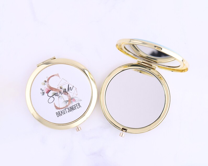 K&ouml;nnte beinhalten: Goldener Kompakt-Spiegel mit einem wei&szlig;en Deckel, der mit einem Blumendesign und dem Text "Sarah Brautjungfer" verziert ist. Der Spiegel ist ge&ouml;ffnet und die reflektierende Oberfl&auml;che ist sichtbar.