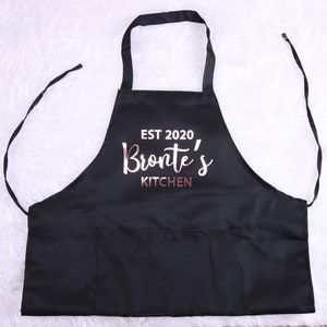 May include: Black kitchen apron with a large pocket and the text "EST 2020 Bronte's KITCHEN" in rose gold lettering.