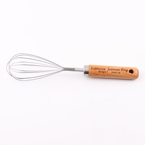 May include: A silver whisk with a wooden handle. The handle is engraved with the text "Subtronics Solomon King Boogie T Level Up".