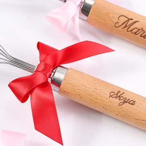 May include: Two wooden handled whisks with red and pink satin bows. The handles are engraved with the names "Skaya" and "Maria".