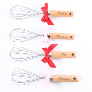 May include: Four silver wire whisks with wooden handles, each handle is personalized with a name. The handles are decorated with red and pink bows.