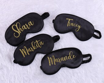 Op de afbeelding: Vier zwarte satijnen slaapmaskers met gouden glitterletters. De namen "Shara", "Markita", "Marande" en "Tracey" staan op de maskers.