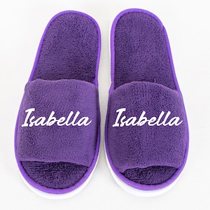 Può includere: Un paio di pantofole viola con testo ricamato bianco che recita "Isabella".