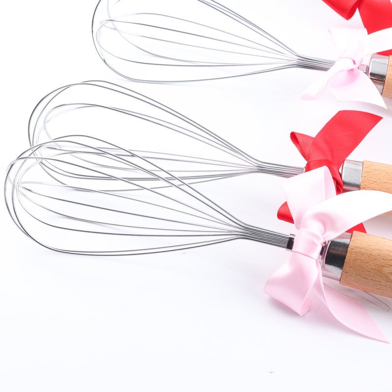 May include: Three silver wire whisks with wooden handles and pink and red ribbon bows.