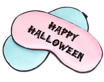 May include: Two eye masks, one pink and one light blue, are stacked. The pink mask features the words "HAPPY HALLOWEEN" in black, gothic lettering with spiderweb details. The masks have black edging, perfect for a spooky Halloween.