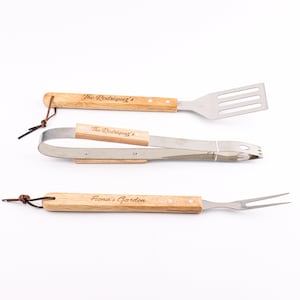Puede incluir: Un juego de tres utensilios para barbacoa de acero inoxidable y madera: una espátula, unas pinzas y un tenedor. Los mangos de madera están grabados con "The Rodriguez's" y "Fiona's Garden". Cada herramienta tiene un lazo de cuero.