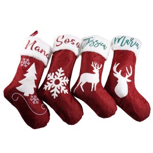 May include: Four red Christmas stockings with white faux fur cuffs. Each stocking has a different design: a Christmas tree, a snowflake, a deer, and a deer head. Names are embroidered on the cuffs.