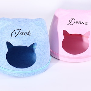 Pode incluir: Duas camas para gatos, uma azul e outra rosa, com os nomes personalizados "Jack" e "Donna" bordados na frente. Cada cama tem uma abertura em forma de gato.