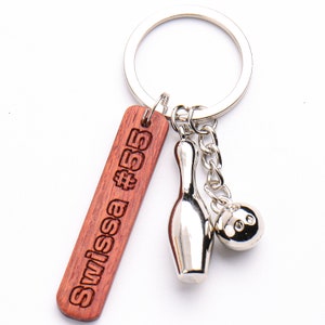 May include: A wooden keychain with the text "Swissa #55" engraved on it. The keychain has a silver metal bowling pin and bowling ball charm attached.