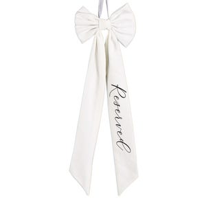 Puede incluir: Un lazo de satén blanco con largas cintas, con la palabra "Reserved" en elegante escritura negra. El lazo está atado en la parte superior con un lazo para colgar. Ideal para bodas o eventos especiales.